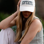 Woman wearing a white cap with 'ESTATE' embroidery sitting outdoors.