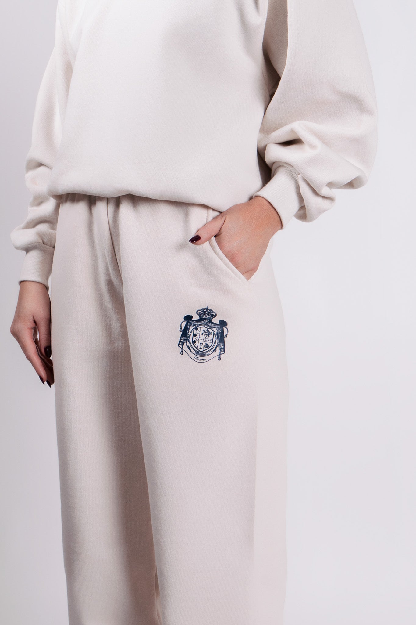 Close-up of Thorne Estate crest embroidery on the cream sweatpant